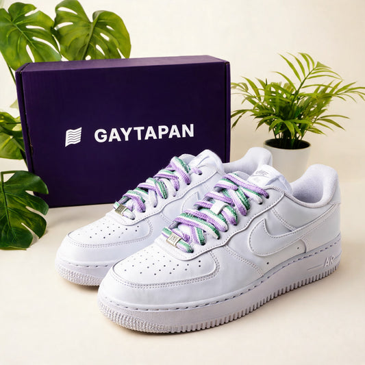 Lacets genderqueer lavande, blanc et vert lacés sur des baskets blanches, boîte GAYTAPAN à l'arrière-plan