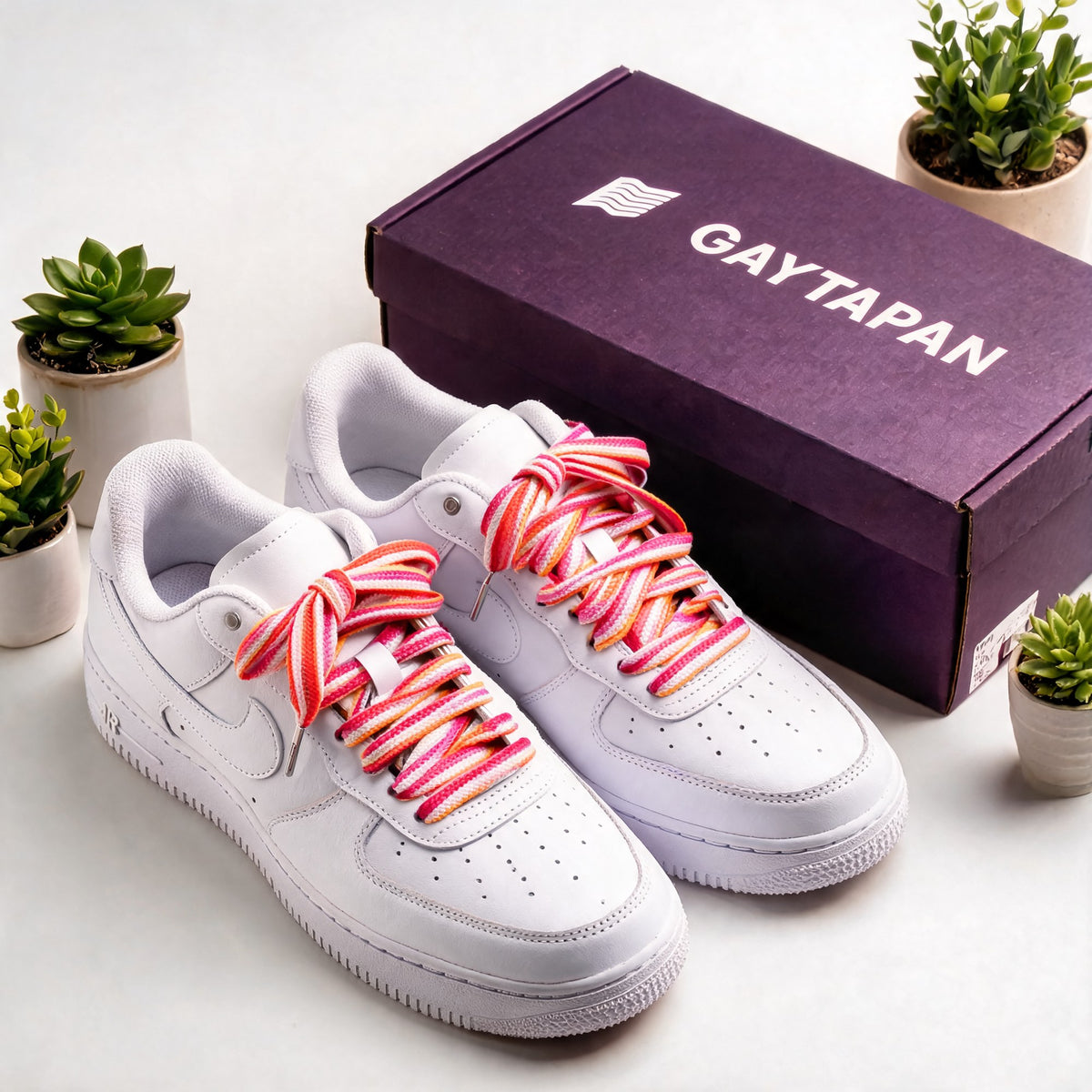 Lacets lesbiens orange, blanc et roses lacés sur des baskets blanches, à côté d'une boîte GAYTAPAN