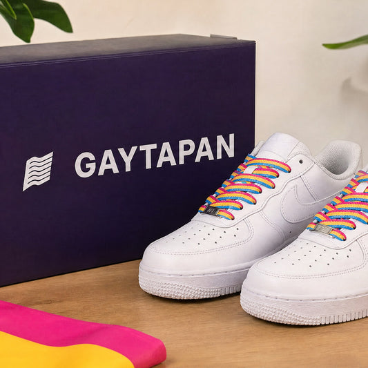 Lacets pansexuels rose, jaune et bleu lacés sur des baskets blanches, avec le drapeau pansexuel et une boîte GAYTAPAN