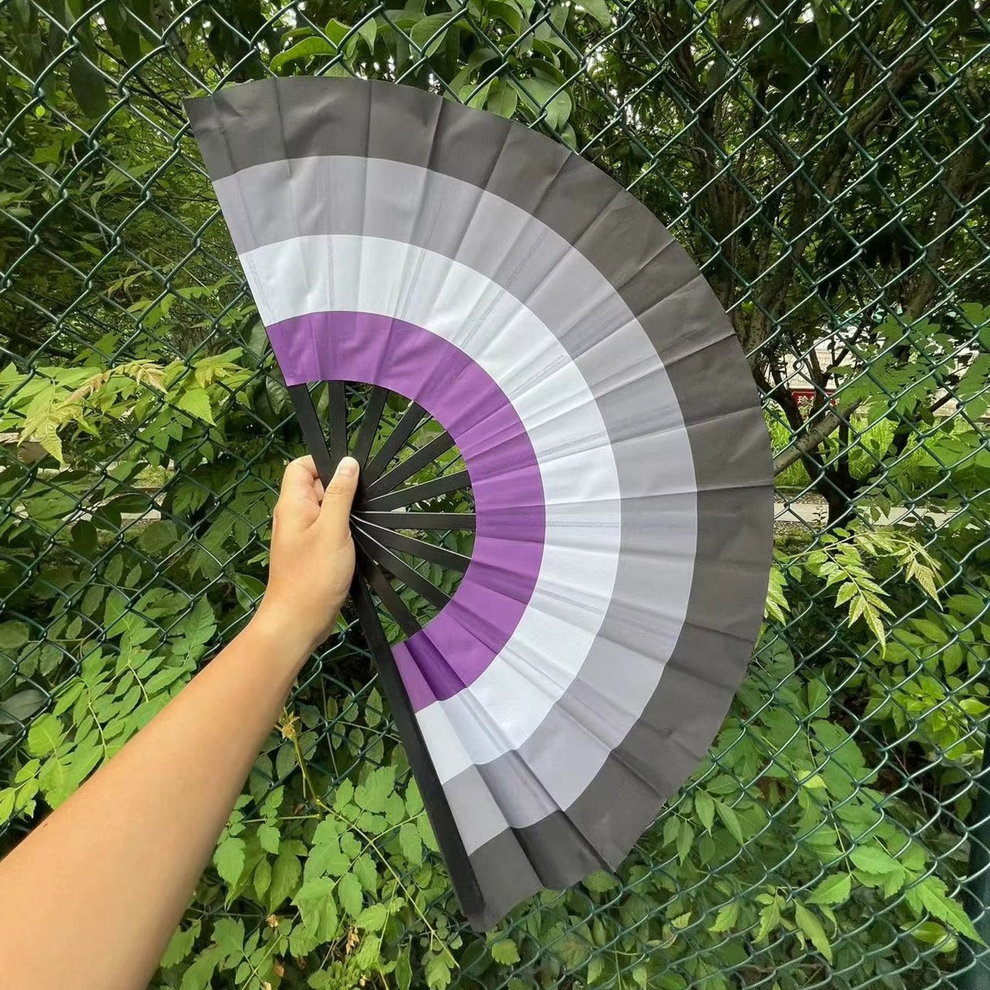 Éventail au drapeau asexuel tenu à la main et déplié — noir, gris, blanc et violet