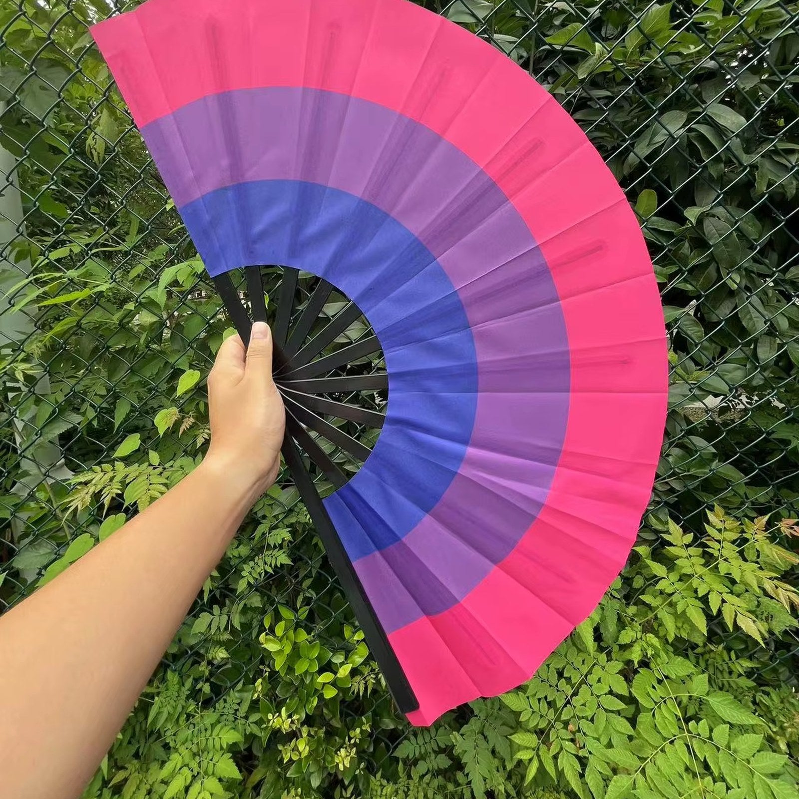 Éventail au drapeau bisexuel tenu à la main et déplié — magenta, lavande et bleu