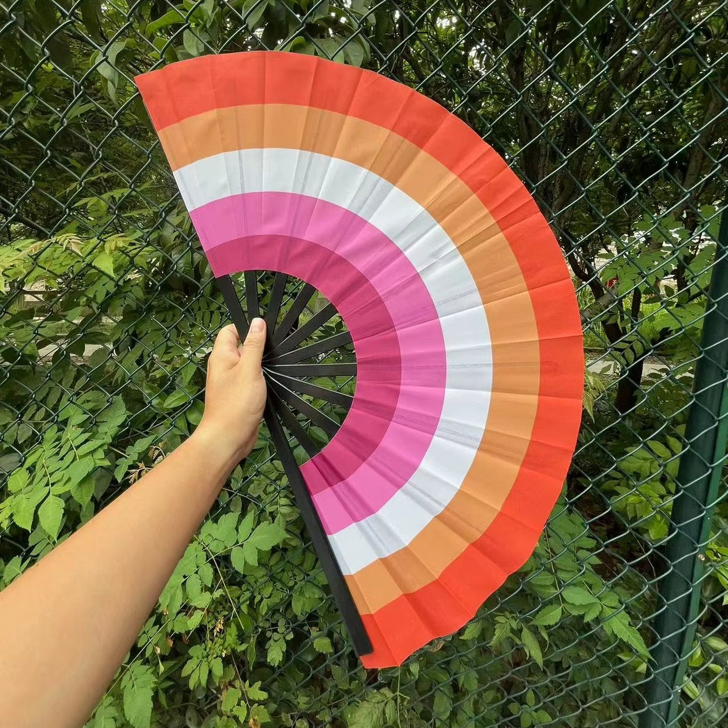 Éventail au drapeau lesbien tenu à la main et déplié — dégradé orange, blanc et rose