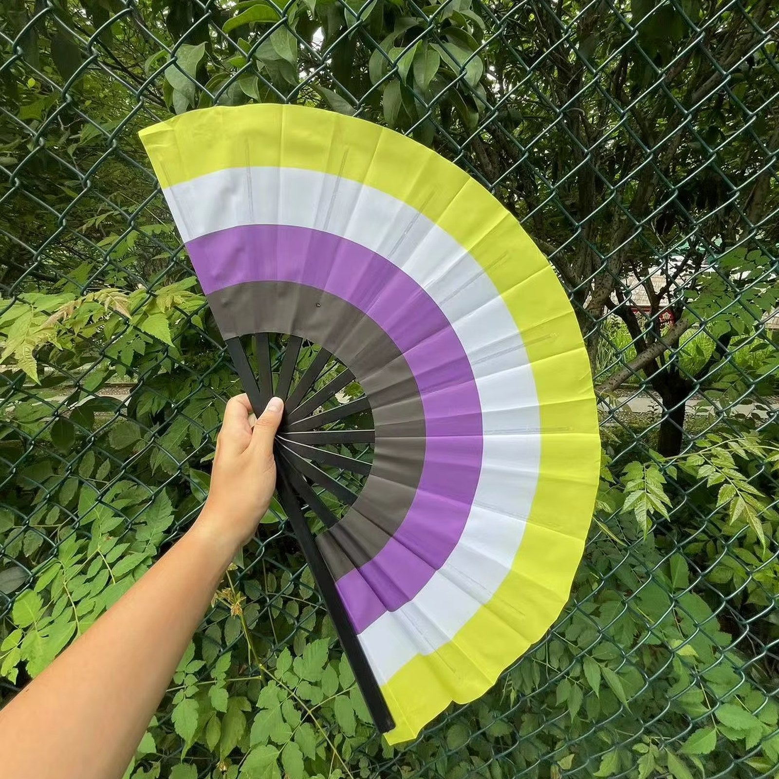 Éventail au drapeau non-binaire tenu à la main et déplié — jaune, blanc, violet et noir