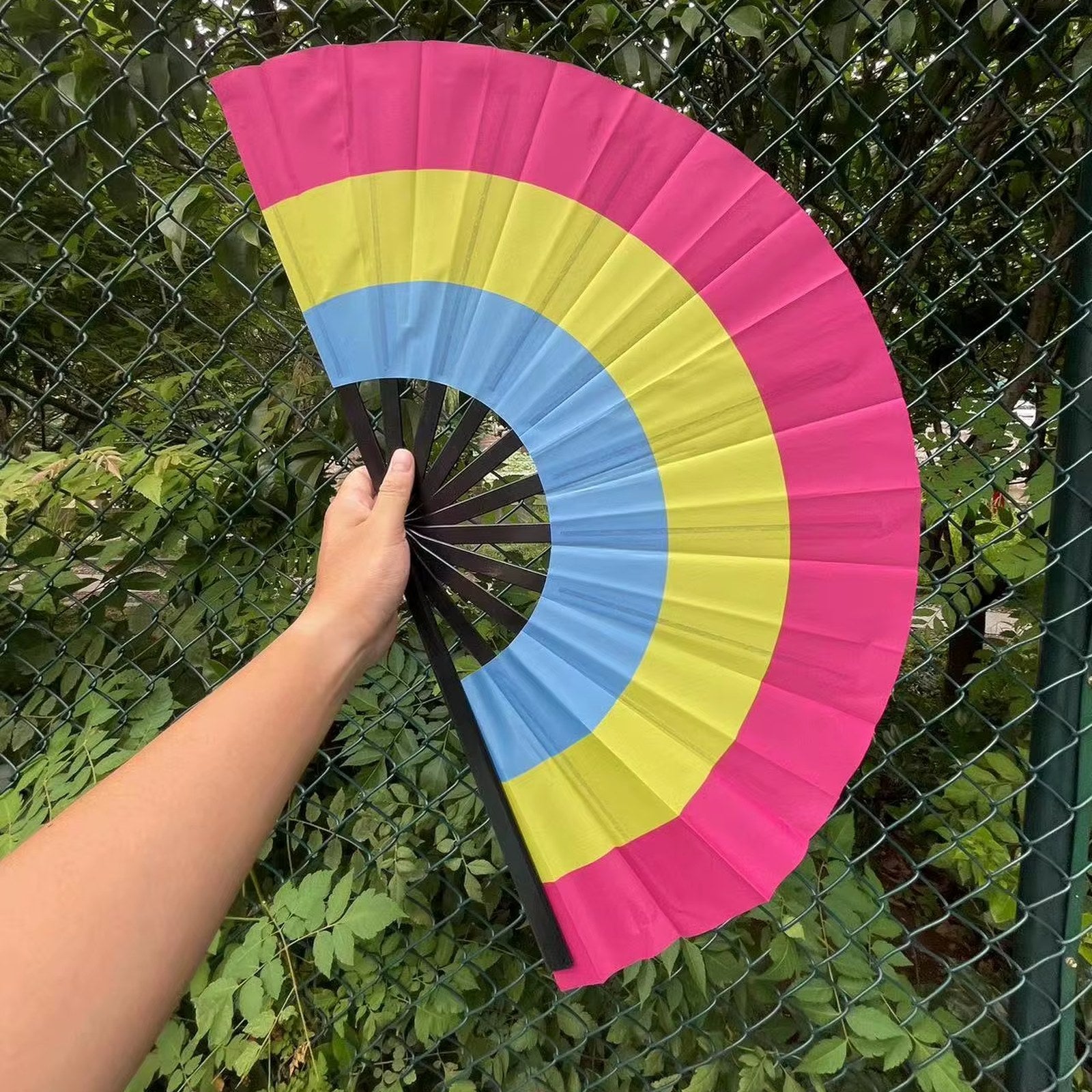 Éventail au drapeau pansexuel tenu à la main et déplié — rose, jaune et bleu
