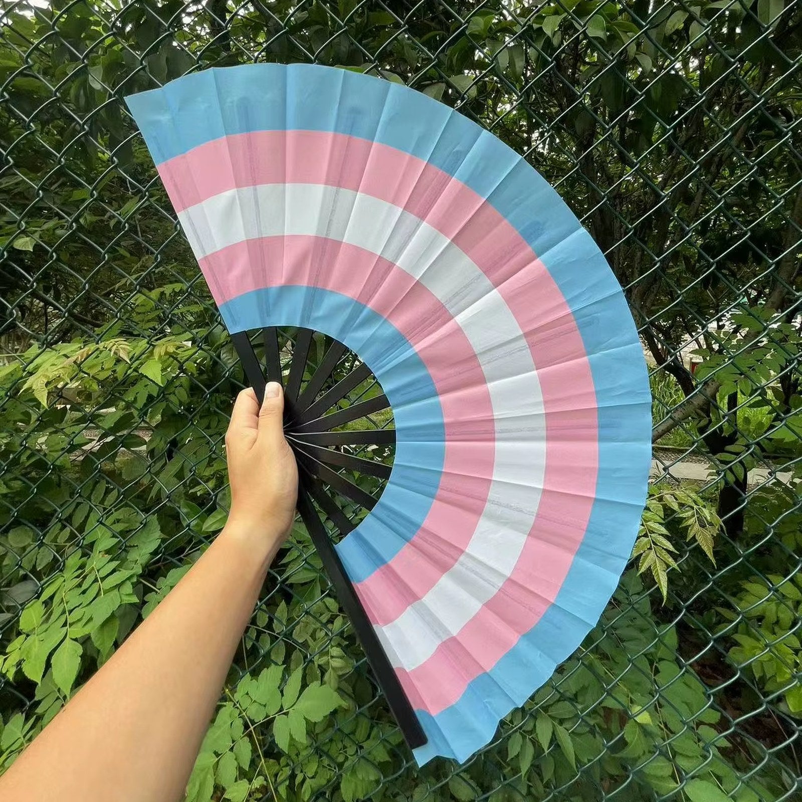 Éventail au drapeau transgenre tenu à la main et déplié — bleu ciel, rose et blanc